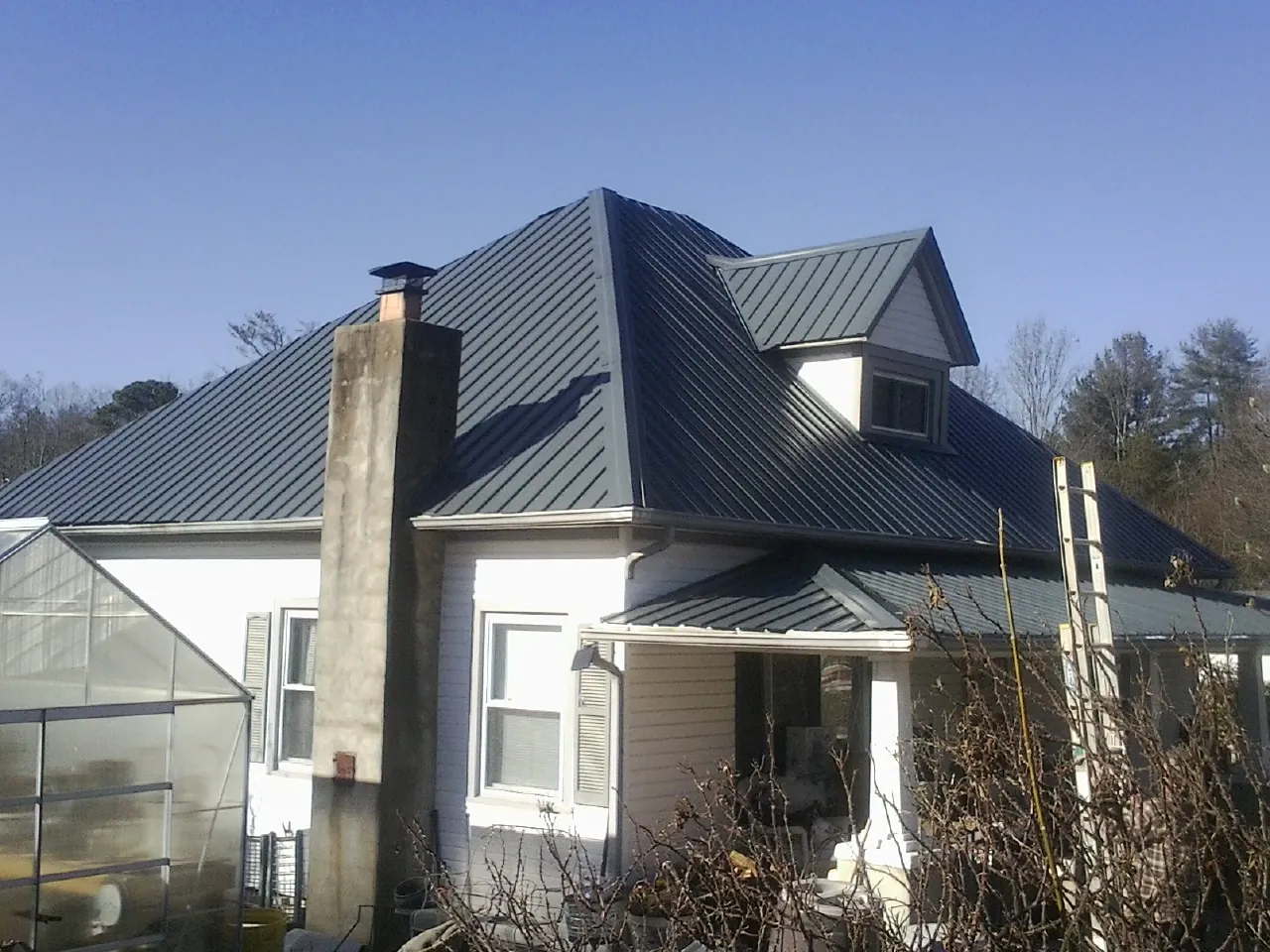 Dark blue standing seam metal roof on a white farmhouse with dormer — Slate & Tile Roof Repair by Roofing Brothers in Groveton