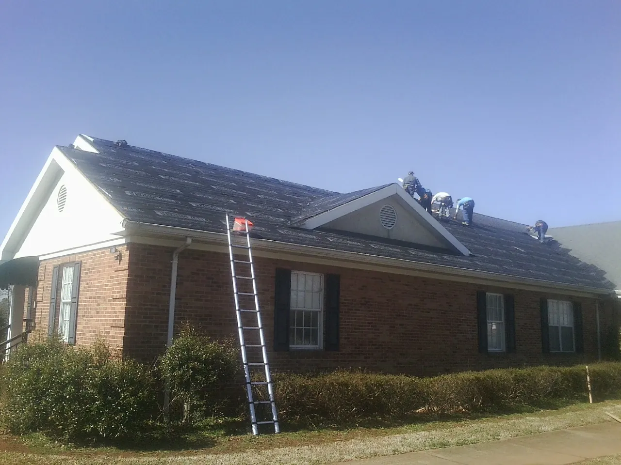 Crew tearing shingles off a brick ranch roof with a ladder set — Emergency Roof Repair work by our crew in Groveton