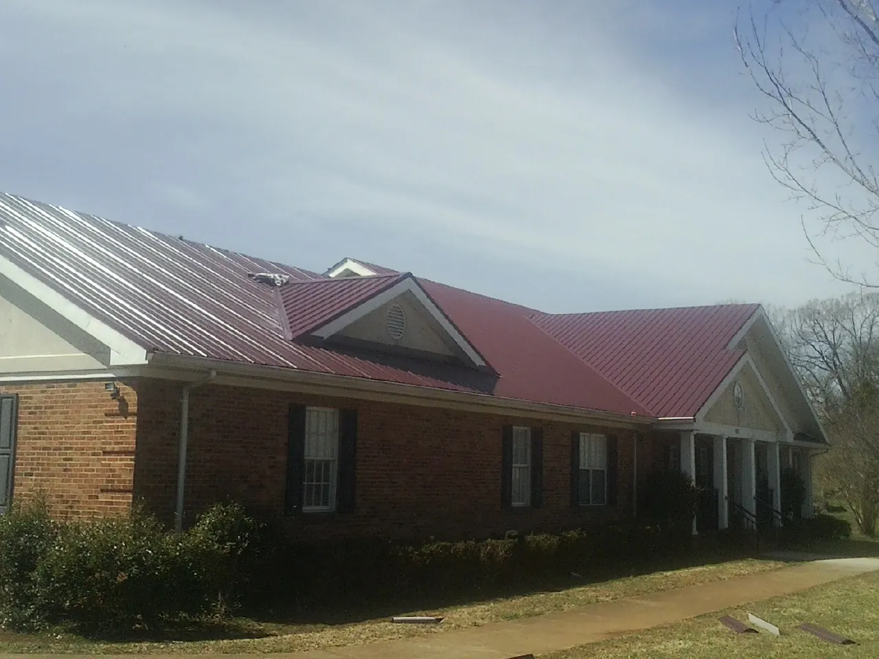 Red metal roof with gabled entries on a long brick building, from a Hail Damage Roof Repair job in Groveton