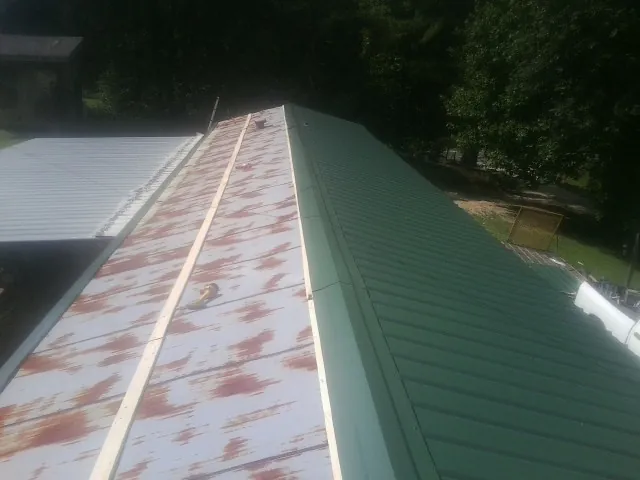 Old rusted panels beside newly installed green metal roofing — Wind Damage Roof Repair by Roofing Brothers in Groveton