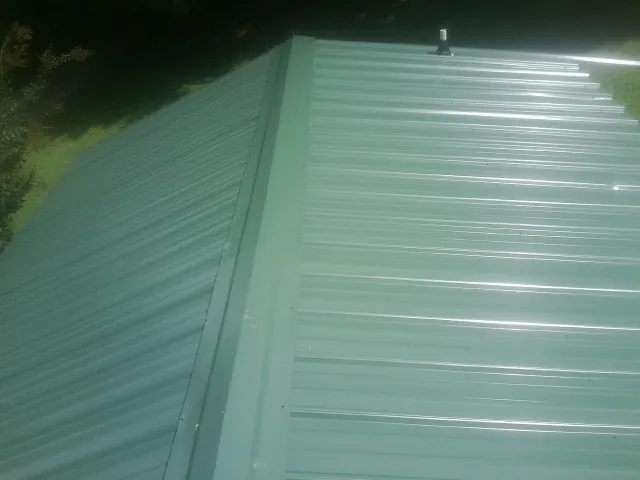 New green metal panels meeting at the ridge of a roof — Flat Roof Repair work by our crew in Groveton