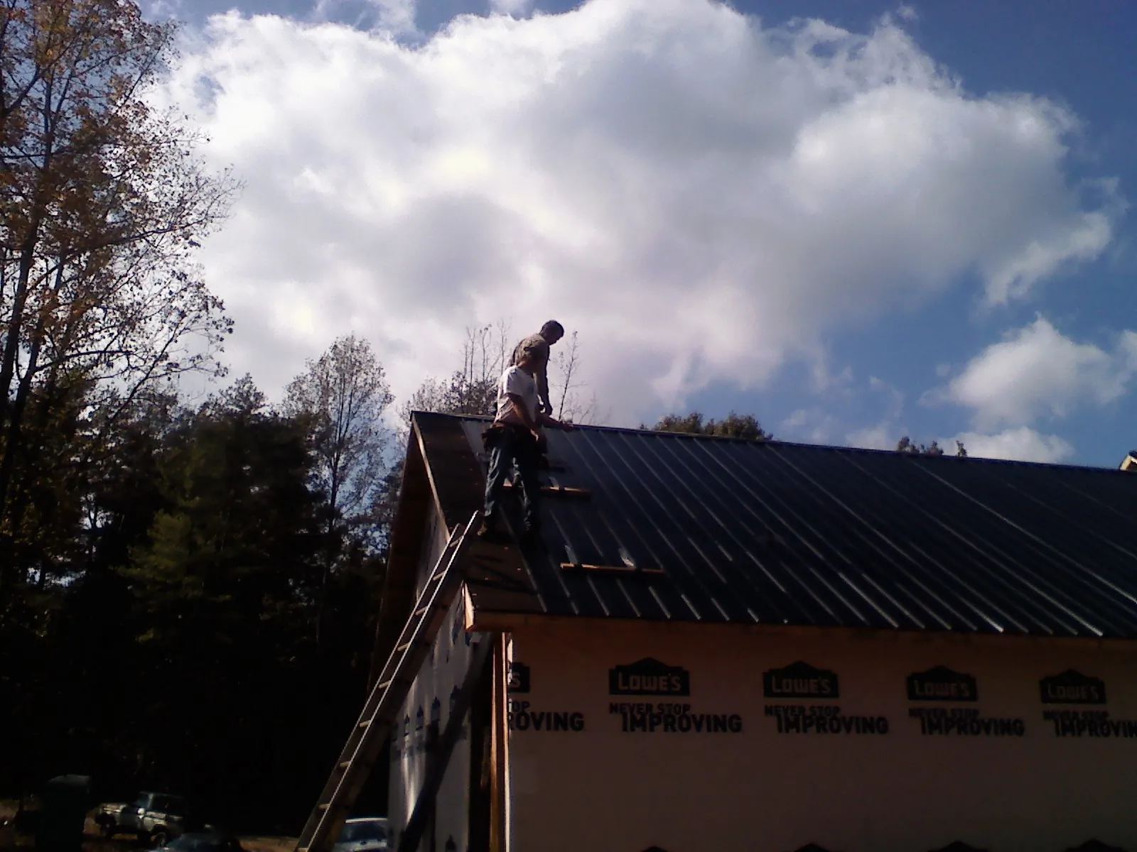 Roofer fastening dark metal panels high against a cloudy sky, from a Roof Inspection job in Groveton