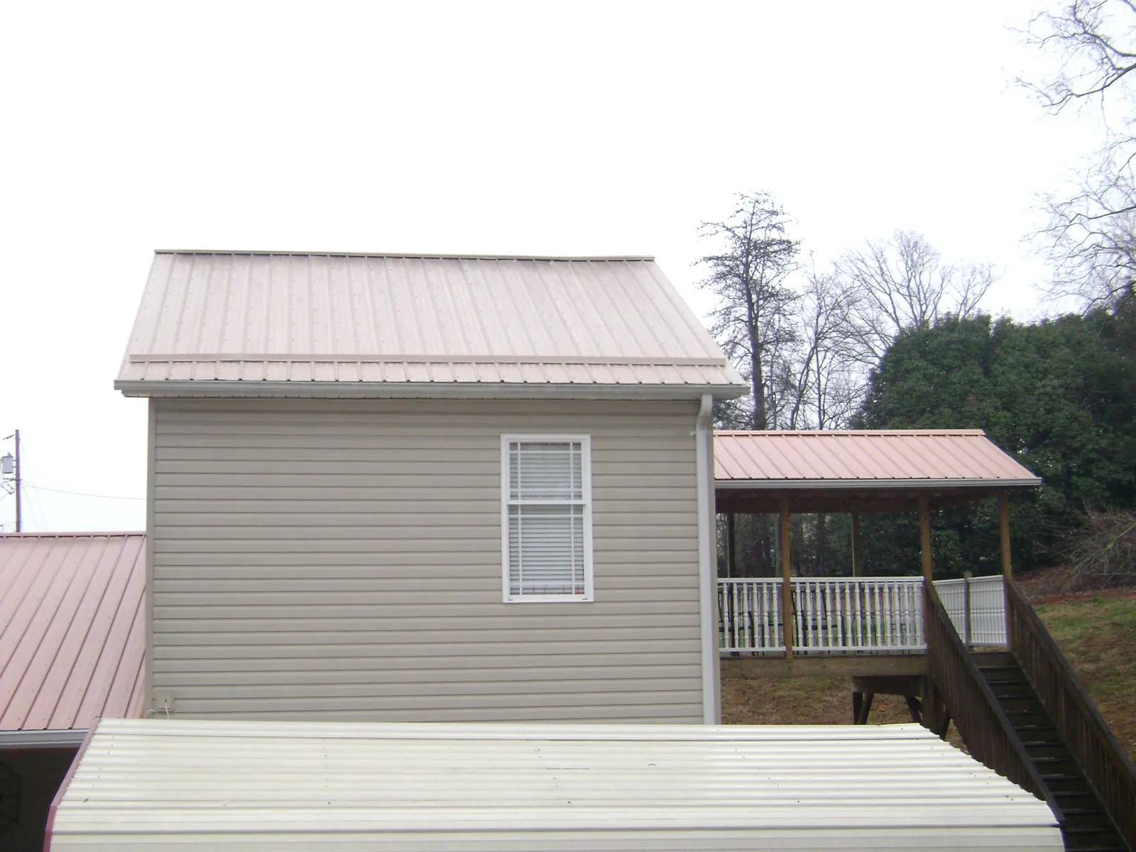Tan metal roofs on a two story addition and attached porch, from a Roof Replacement job in Groveton