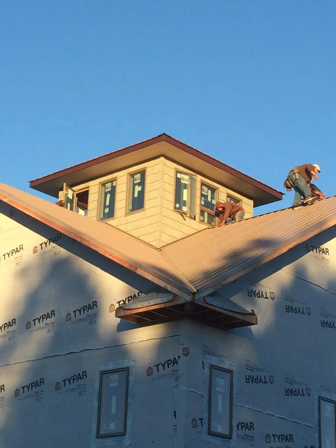 Roofers working around a rooftop cupola on a new metal roof at sunset — Roof Waterproofing in Groveton by Roofing Brothers
